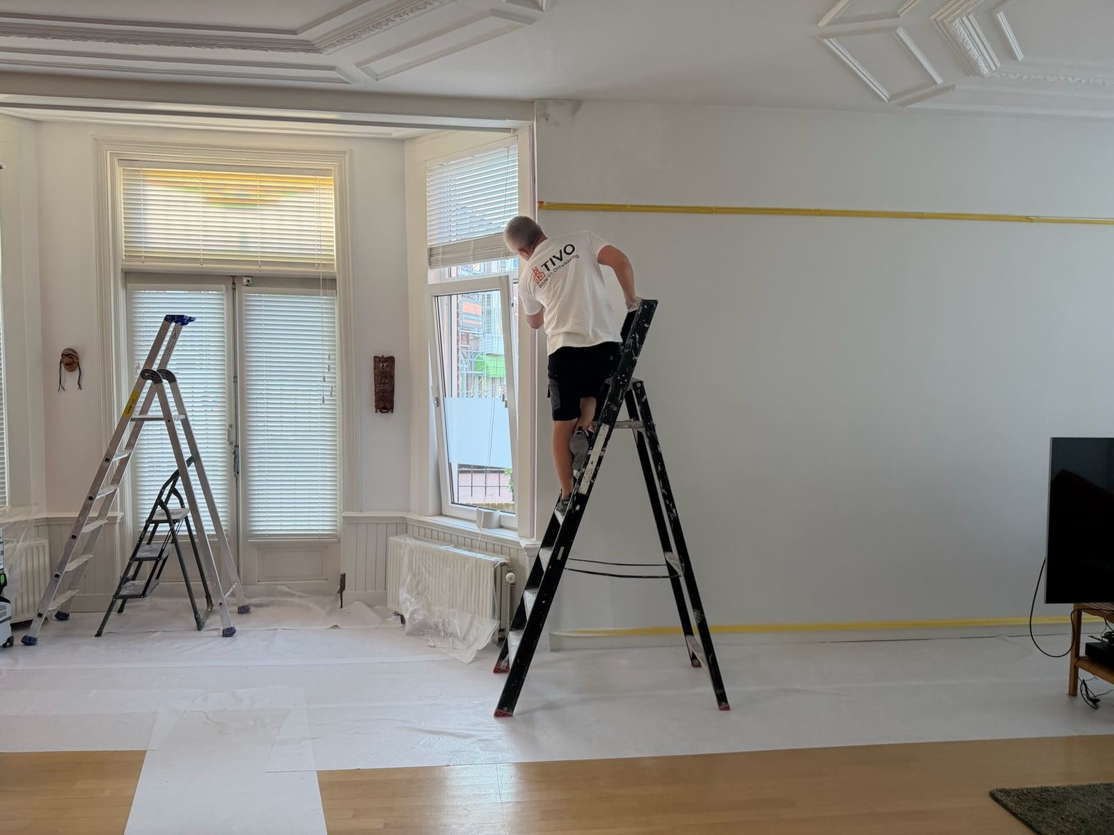 Schilderwerk in een klassieke kamer met sierlijstwerk, met de vloer volledig afgedekt