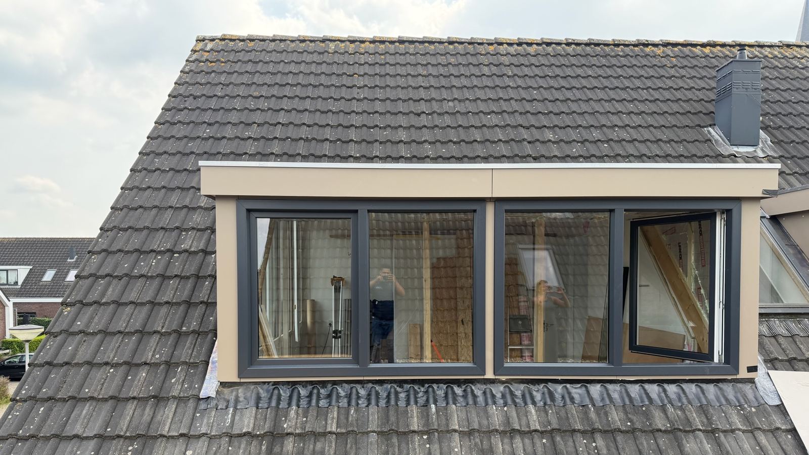 De brede dakkapel van buiten, afgewerkt met antracieten kozijnen en een crème boeiboord