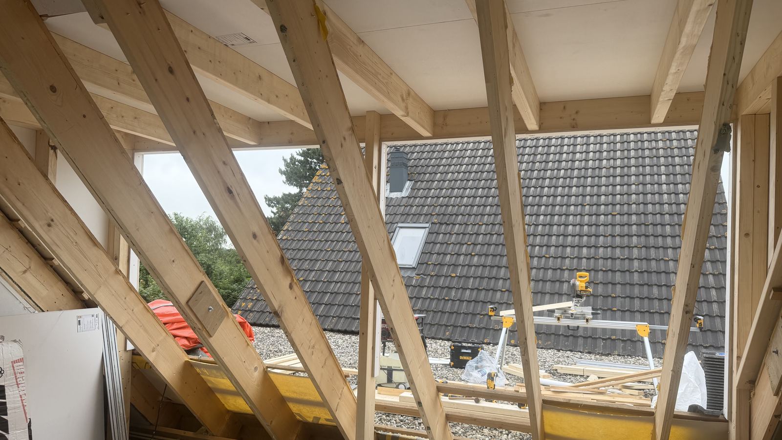 De dakkapelopening van binnenuit, nog in het kale houten stijlwerk, met uitzicht op het pannendak