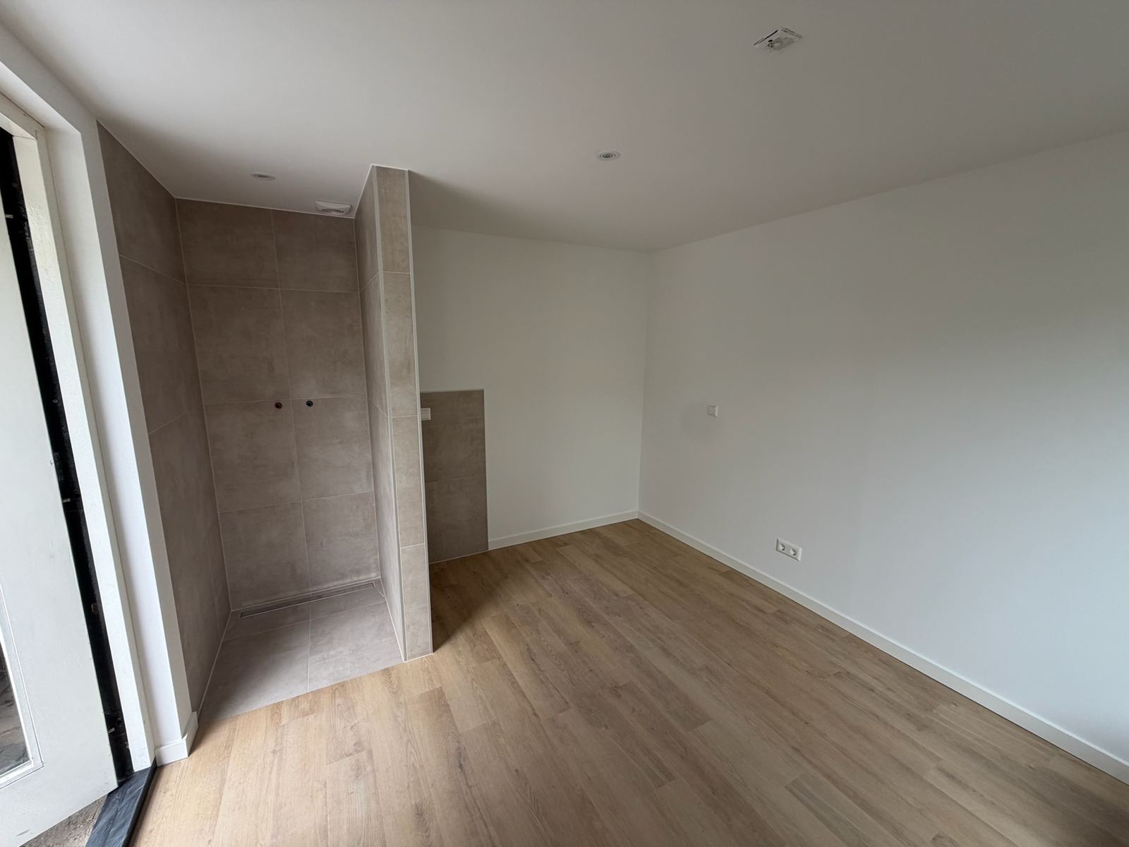 Afgewerkte slaapruimte met houtlook vloer en de betegelde doucheruimte ernaast
