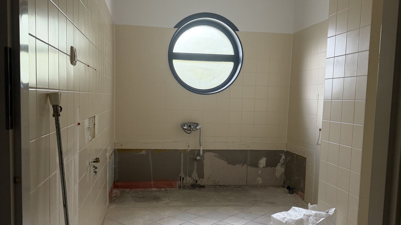 De oude badkamer met beige tegelwerk en het ronde raam, vóór de renovatie
