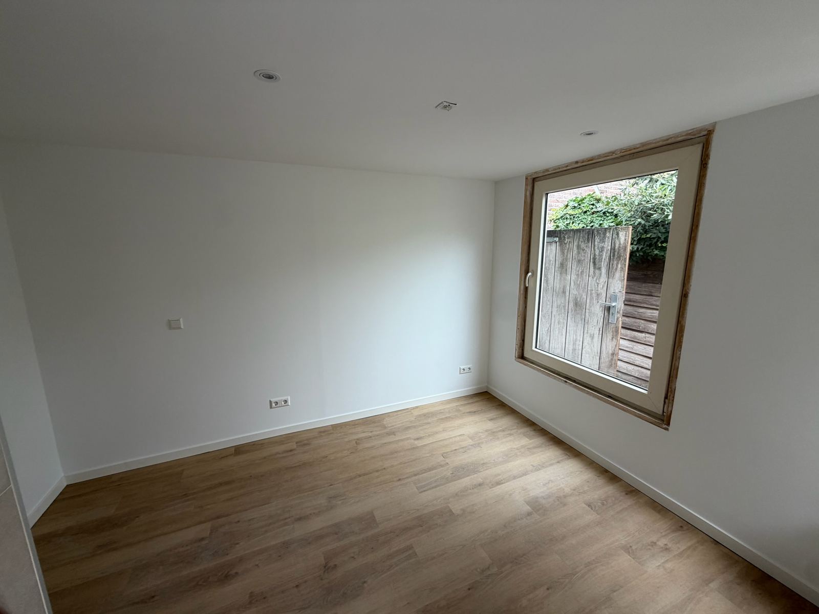 Afgewerkte ruimte met houten vloer en een houten kozijn dat op de tuin uitkijkt